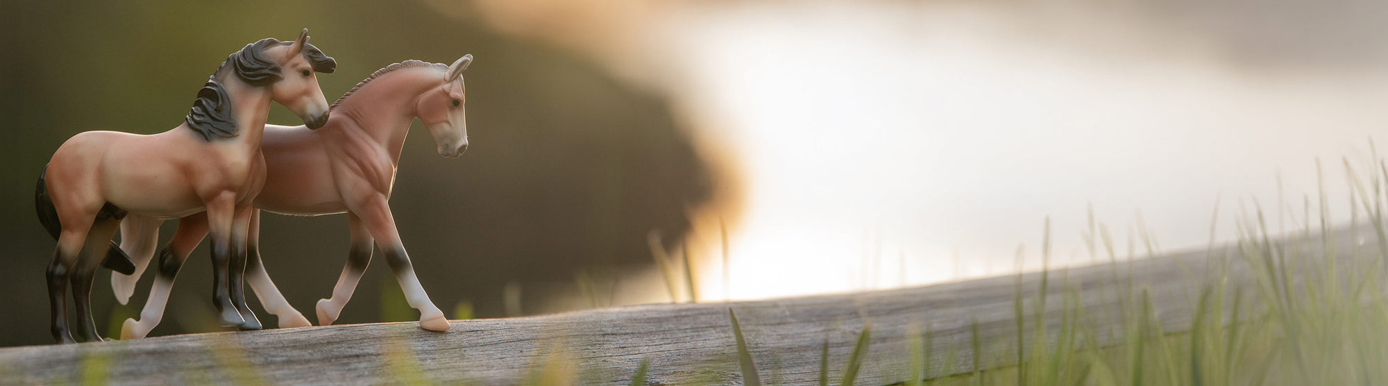 Two Breyer Stablemates standing side-by-side on a log overlooking a river
