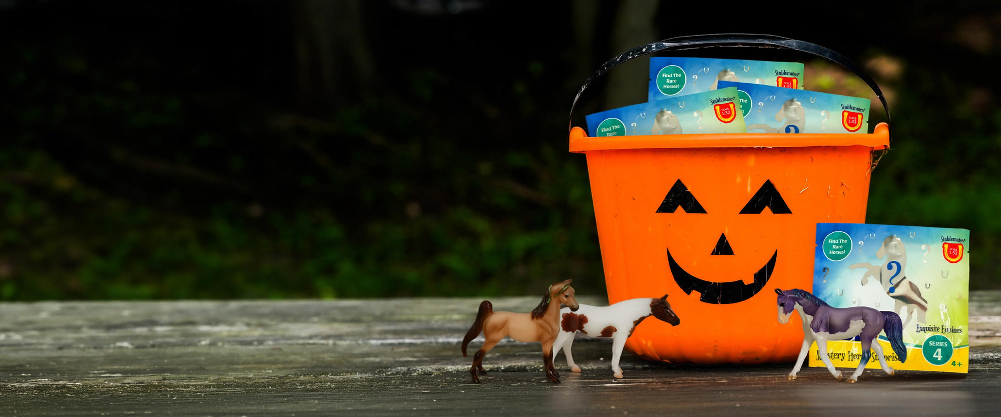 Breyer Blind Bags in a trick-or-treating pumpkin bucket on a table outside with 3 Stablemates unwrapped.