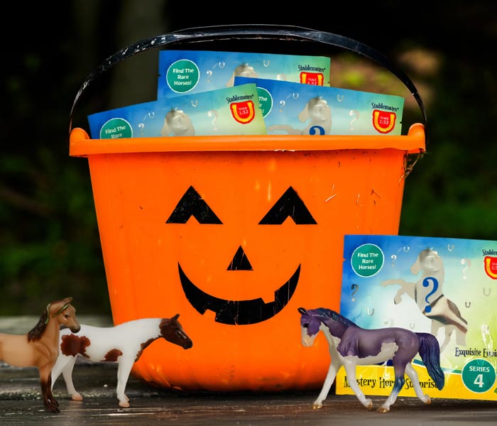 Breyer Blind Bags in a trick-or-treating pumpkin bucket on a table outside with 3 Stablemates unwrapped.