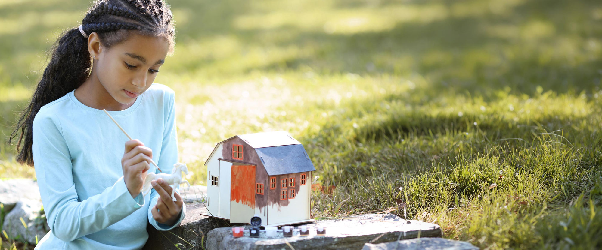 A child painting a Breyer model horse and barn outside