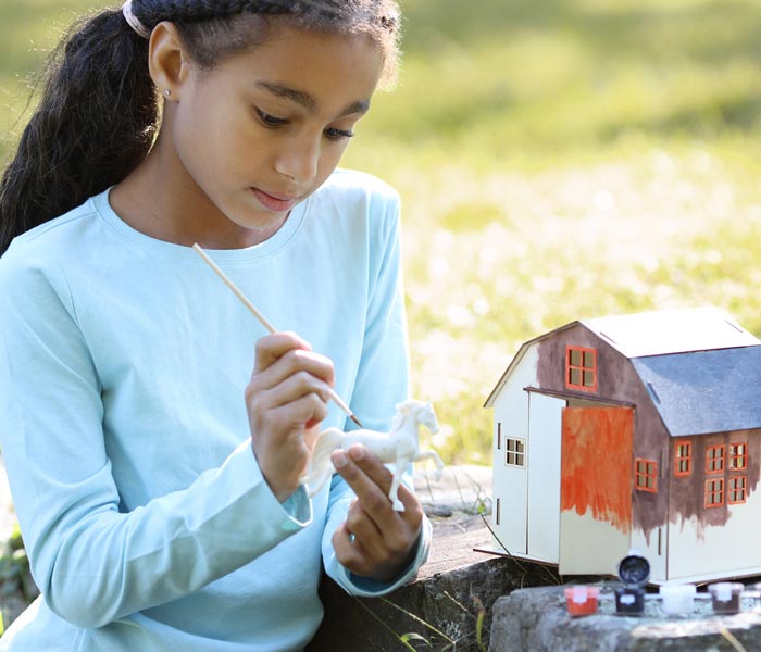 A child painting a Breyer model horse and barn outside
