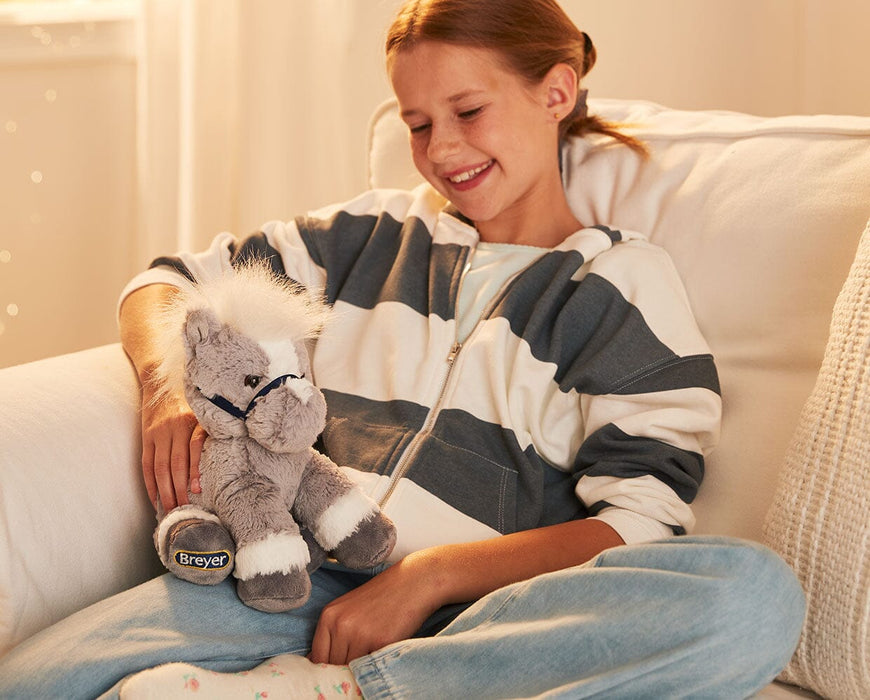 A child holding the 11" Grey Horse | Bridle Buddies sitting on a couch