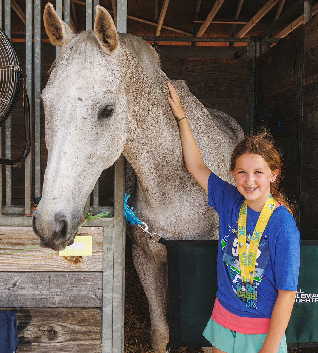 A child petting a horse in a stall at BreyerFest