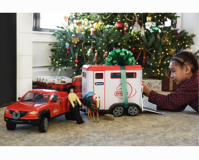 A girl by the Christmas Tree playing with Austin and the Dually Truck and Trailer
