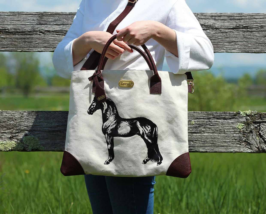 A person with the tote bag next to a fence and field.