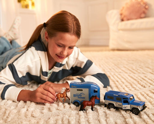 A child playing with the Breyer Farms™ Land Rover® and Tag-A-Long Horse Trailer on the floor
