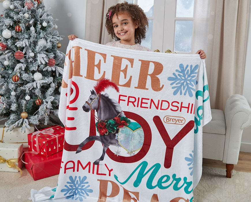 A child holding up the Christmas in Bloom Holiday Throw in front of a Christmas tree.