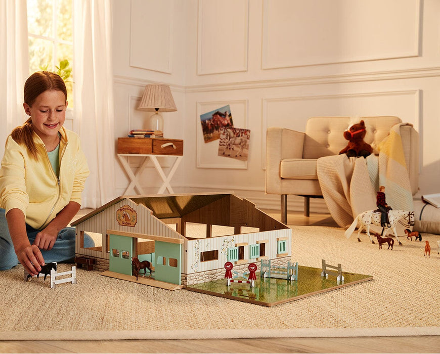 A Girl playing with the Deluxe Arena Stable on a floor with the roof open