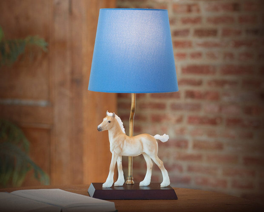 Phoebe on lamp facing left on a a table with a brick wall in the background