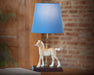Phoebe on lamp facing left on a a table with a brick wall in the background